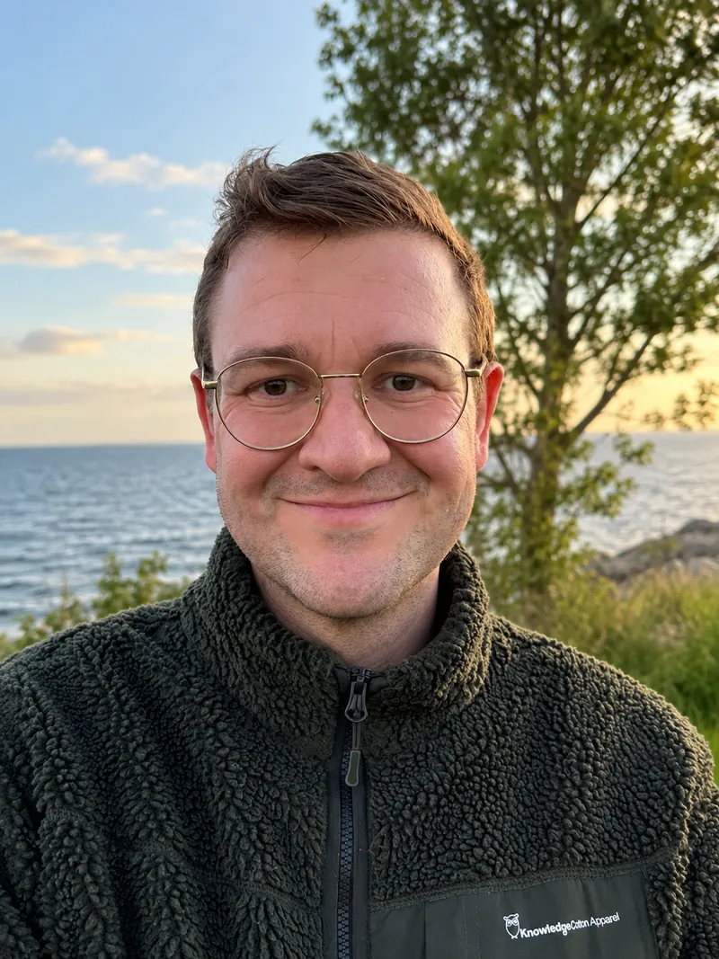 Hjalte Daniel outdoors by the water, wearing glasses and a dark fleece.